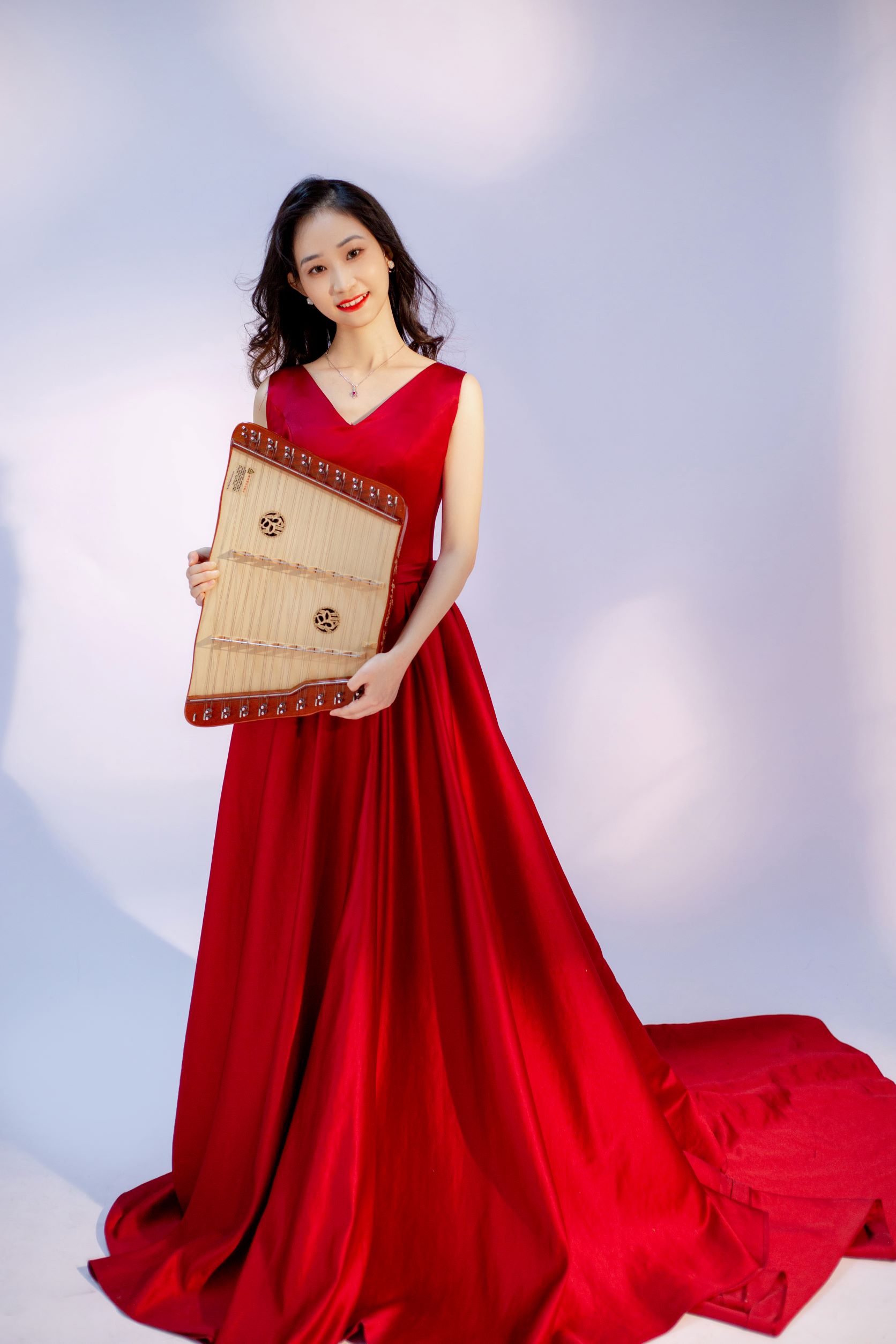 Picture of Liu Lyujing.  She is smiling at the camera while wearing a formal red gown and holding a small zither.